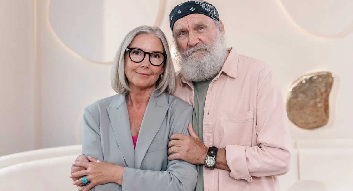 Elderly couple embracing indoors, showcasing fashion and warmth.